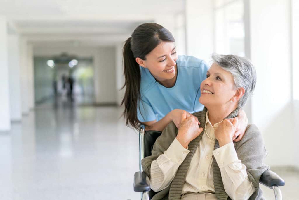 Gesundheits- und Krankenpfleger Aufgaben – Schwester hilft Patientin im Rollstuhl